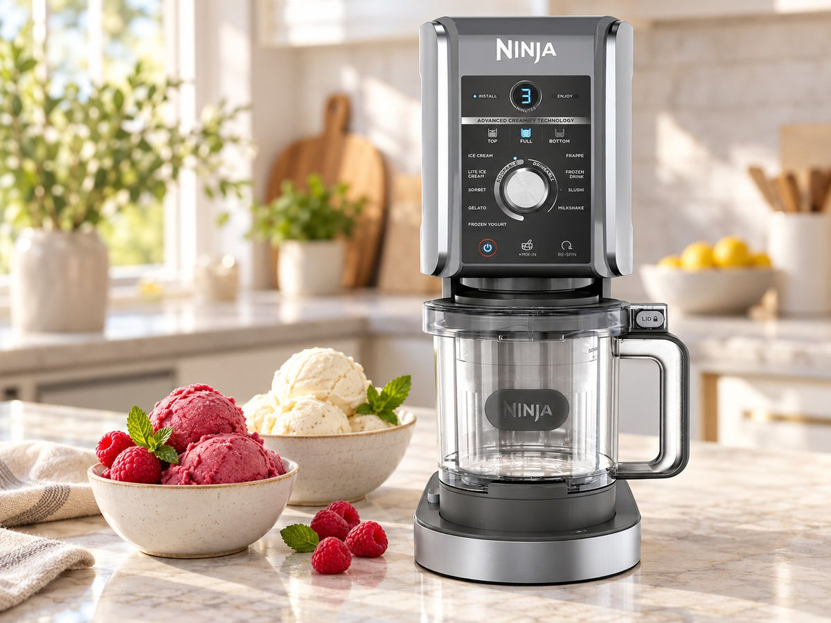 Ninja CREAMi Deluxe NC502EU machine à glace sur un plan de travail, à côté de coupes de glace framboise et vanille